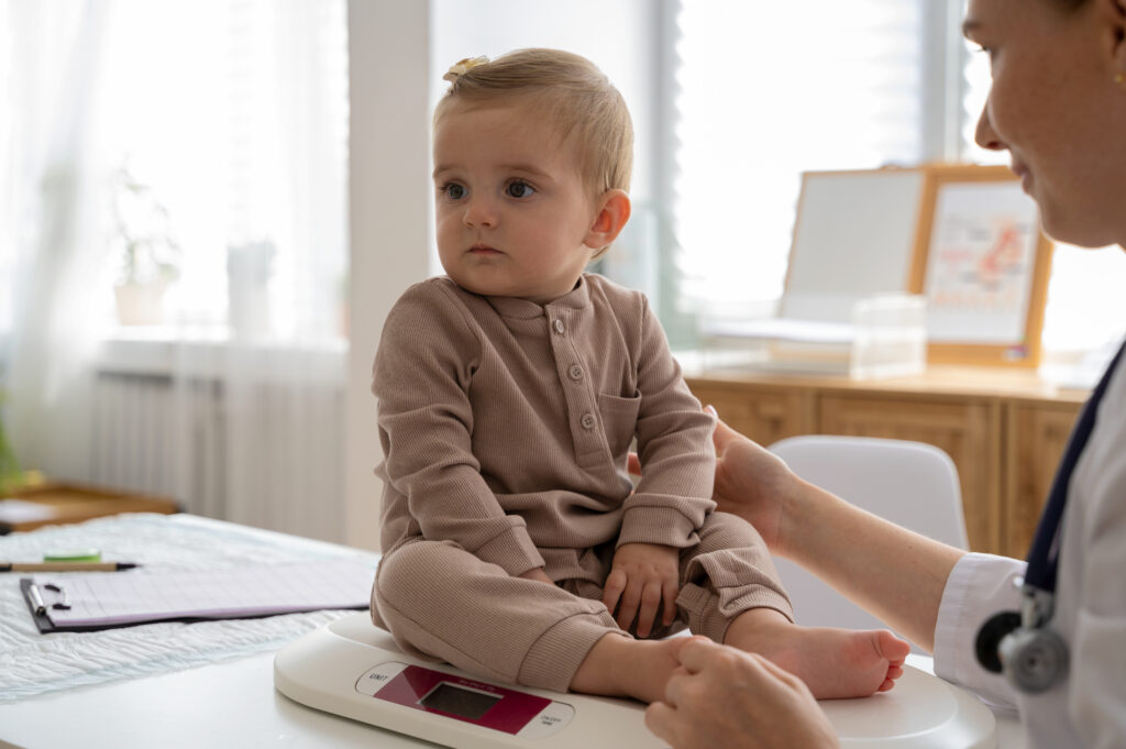 Child in brown outfit being examined by a healthcare professional on a scale.